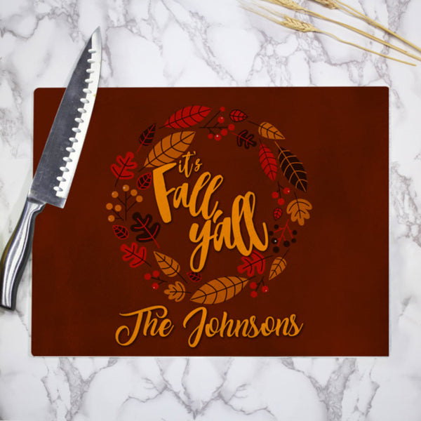 Brown background with earth tones of leaf circular border around it's Fall Y'll text and any personalized text on the bottom of a printed tempered glass cutting board