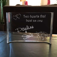 double linked hears along with a kissing couple and text that says "Two hearts that beat as one". Any two names personalized on this curved clear acrylic desk plaque