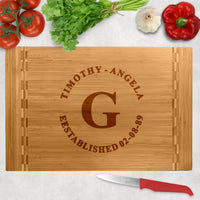 Last Name initial in center with names arched above and establish date below on a butcher block inlay bamboo cutting board
