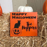 Wood Sign painted orange with black text and design  Cat sitting on pumpkin  Happy Halloween on to and Family Name to the right of the cat/pumpkin