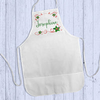 Apron shown lying flat on wood Personalized Apron with holly and ribbon rectangle framing to any name. 