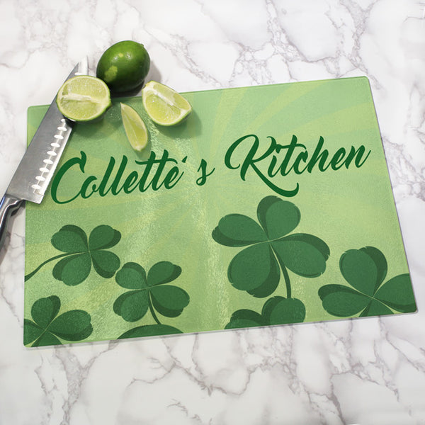 Glass Cutting Board with Soft Green Sun Rays in the background and a scattering of four leaf clovers on bottom. Any Name or custom text personalized towards the top of the cutting board