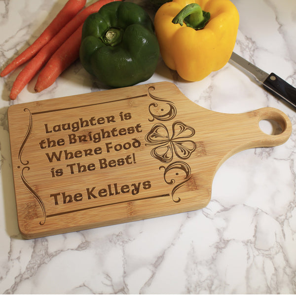 Paddle style cutting board with quote "Laughter is the Brightest Where Food is the Best" and personalized with any name. Stylish border with one shamrock surrounds board and text.