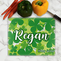 Scatter of Shamrocks fill up the background on a glass cutting board personalized with your name large in the center and an additional line of text small on the bottom right.